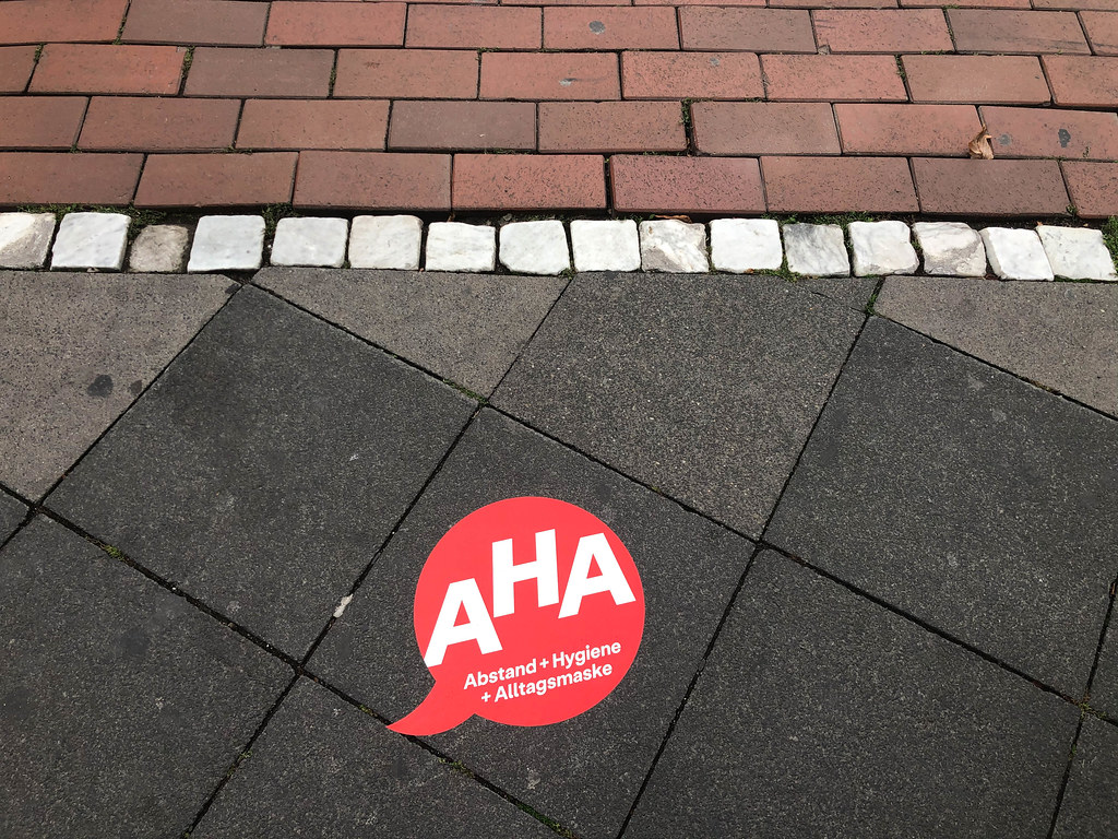 Ein roter Aufkleber mit dem Corona-Mantra AHA (Abstand + Hygiene + Alltagsmaske) auf dem Boden