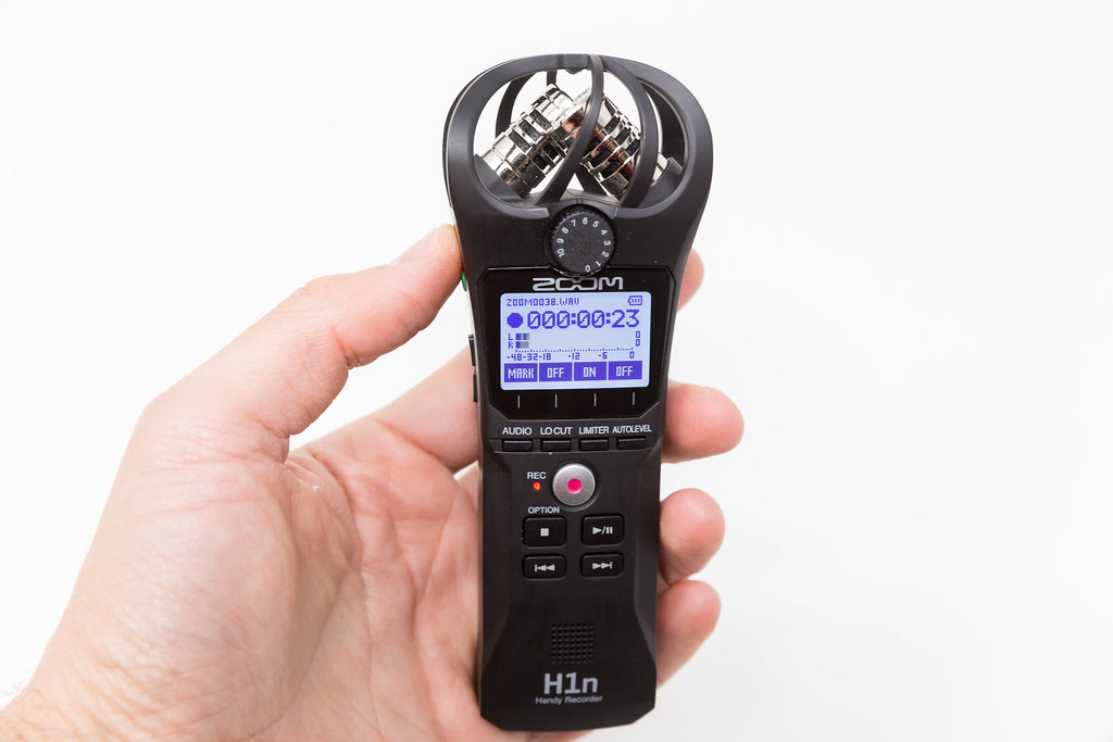 Hand holding the Zoom H1n Handy Recorder while a recording is being shown on the display