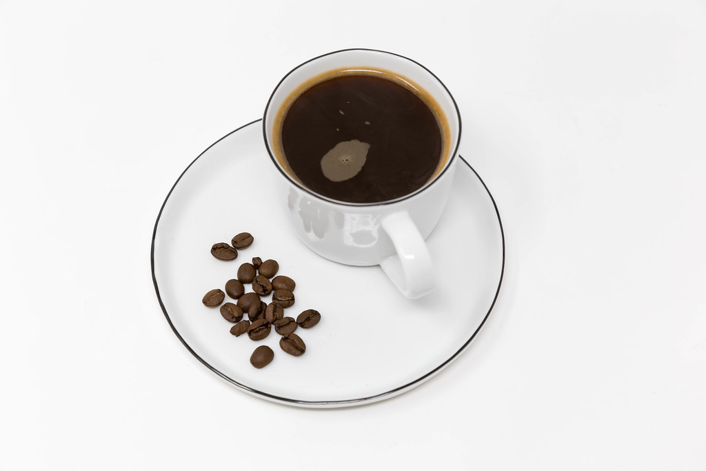 Guten Morgen mit schwarzem Kaffee in einer weißen Tasse mit Kaffeebohnen auf einem weißen Teller