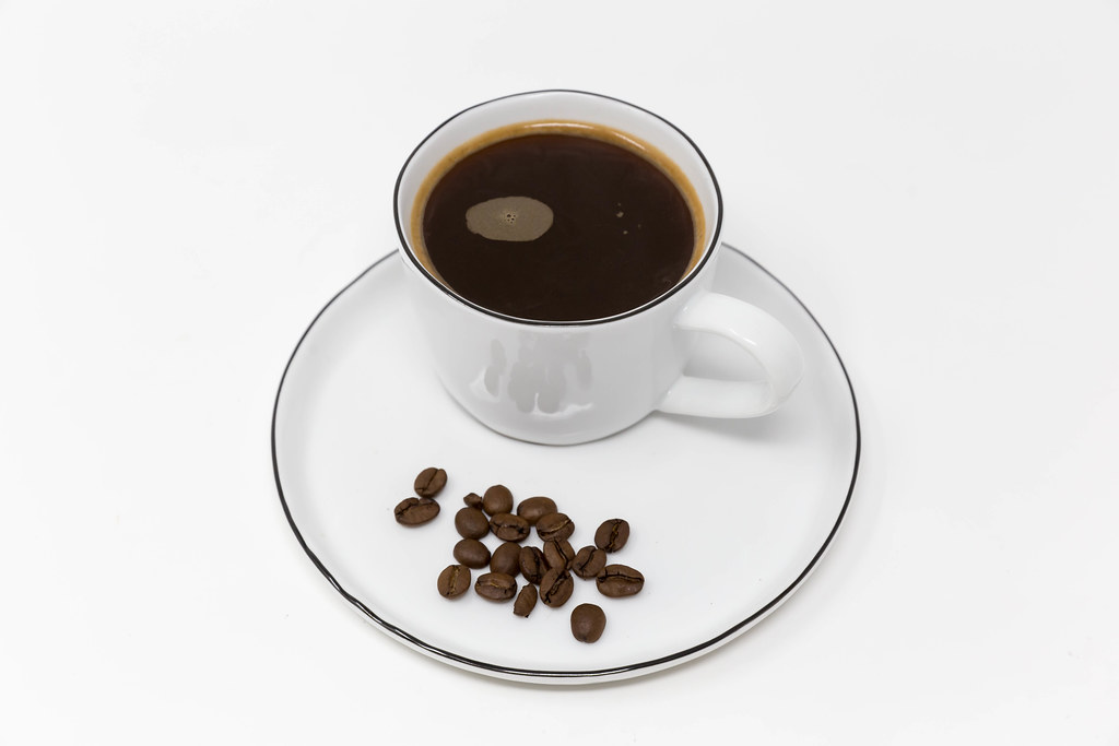 Black coffee cup with no milk served on a white plate with decorative coffee beans and white background