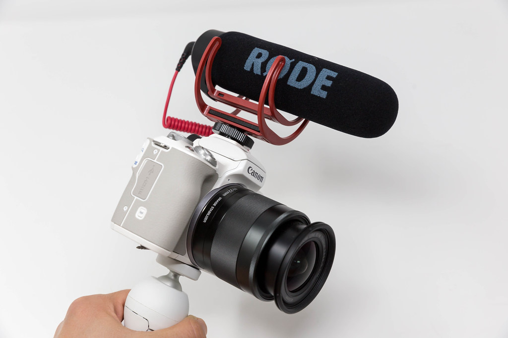Hand hält eine Canon DSLR Kamera mit RØDE kompaktem Mikrofon vor weißem Hintergrund