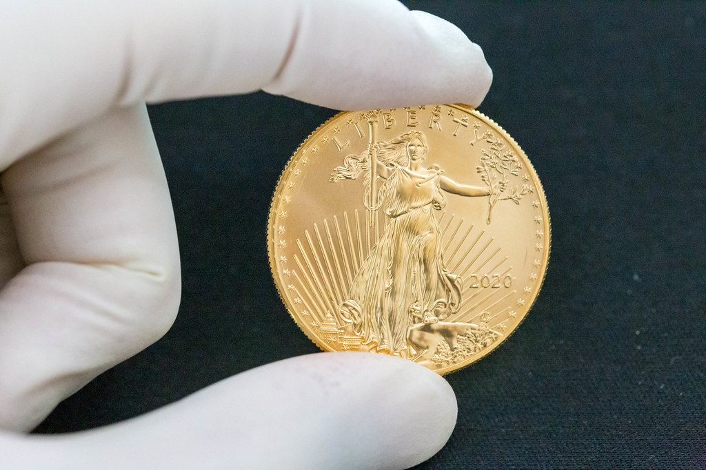 Hand with gloves holds an American Eagle Liberty 2020 gold coin