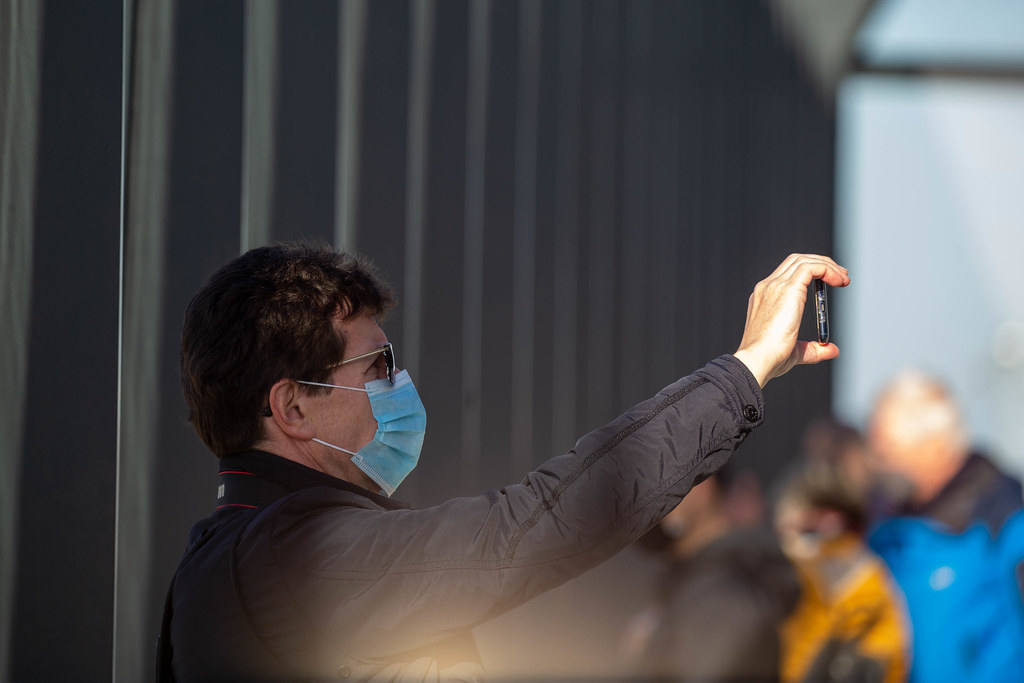 Corona-Zeit: Mann mit OP-Maske fotografiert mit seinem Smartphone am neuen Flughafen BER