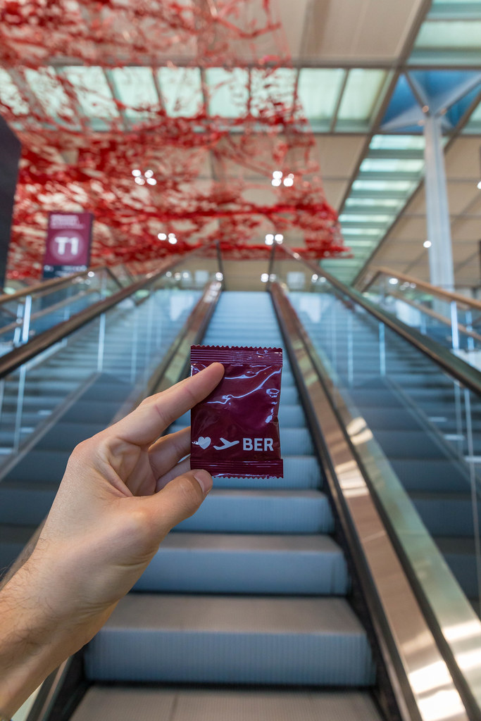 Hand with red gadget of new Berlin airport in front of empty escalators and Pae White's red ceiling artwork