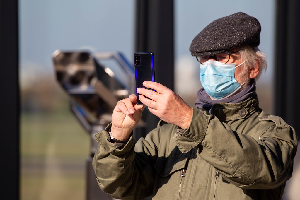 Man with face mask takes a smartphone photo from the visitor terrace of the new Berlin airport BER
