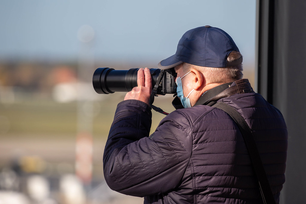 Man with face mask and camera with zoom lens takes photos from the BER airport visitor terrace