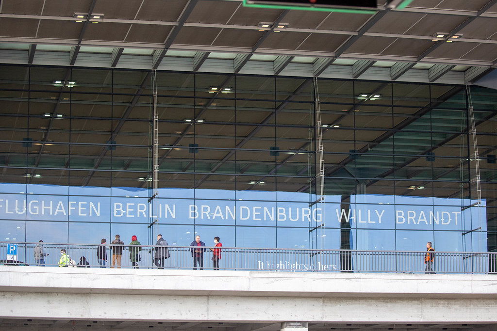 Menschen vor dem BER Terminal 1 mit Schrift auf Glas 