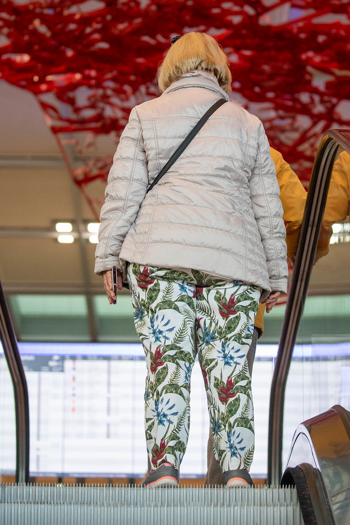 Eine Frau auf der Rolltreppe vom neuen Flughafen BER mit Pae Whites rotem Kunstwerk im Hintergrund