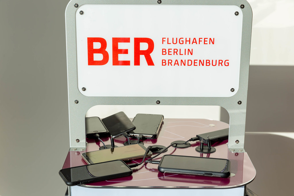 Six mobile phones and a power bank being charged at a charging station with logo of the BER airport