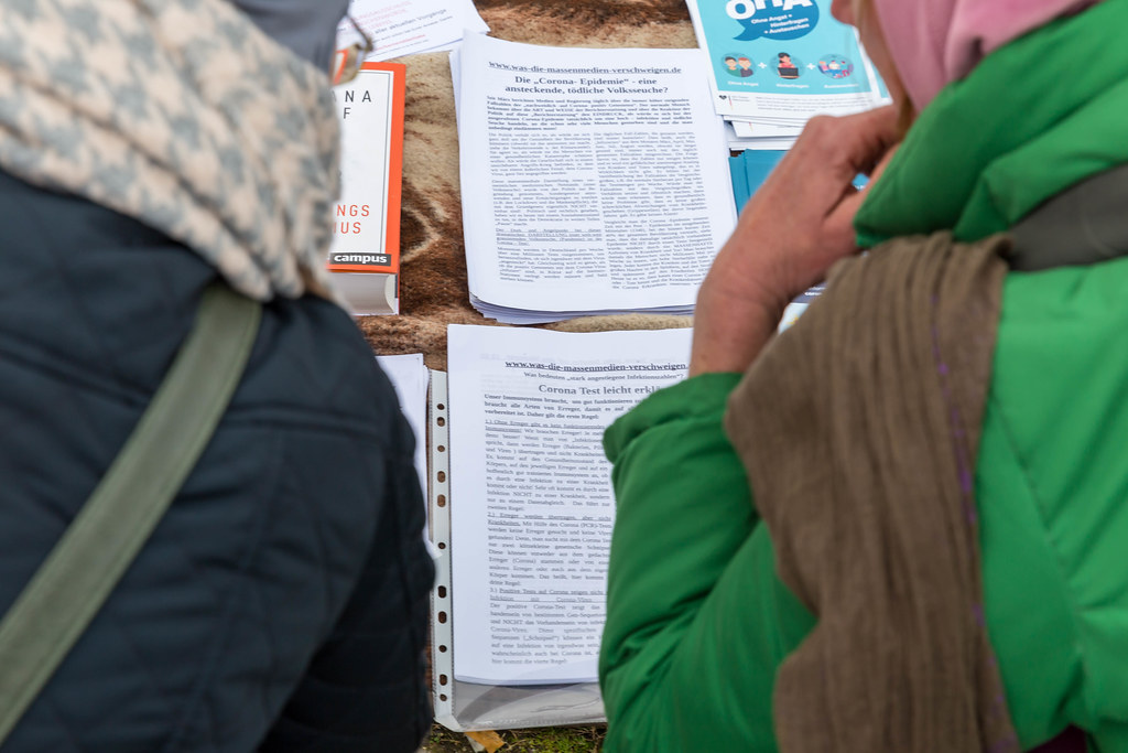 Two participants demo over anti-Covid measures read printed pamphlets on conspiracy theories