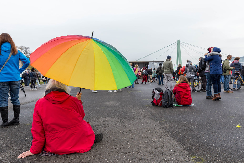 Deutzer Werft, Köln: Frau mit Regenbogenschirm und rote Jacke bei Demo gegen Corona-Regeln