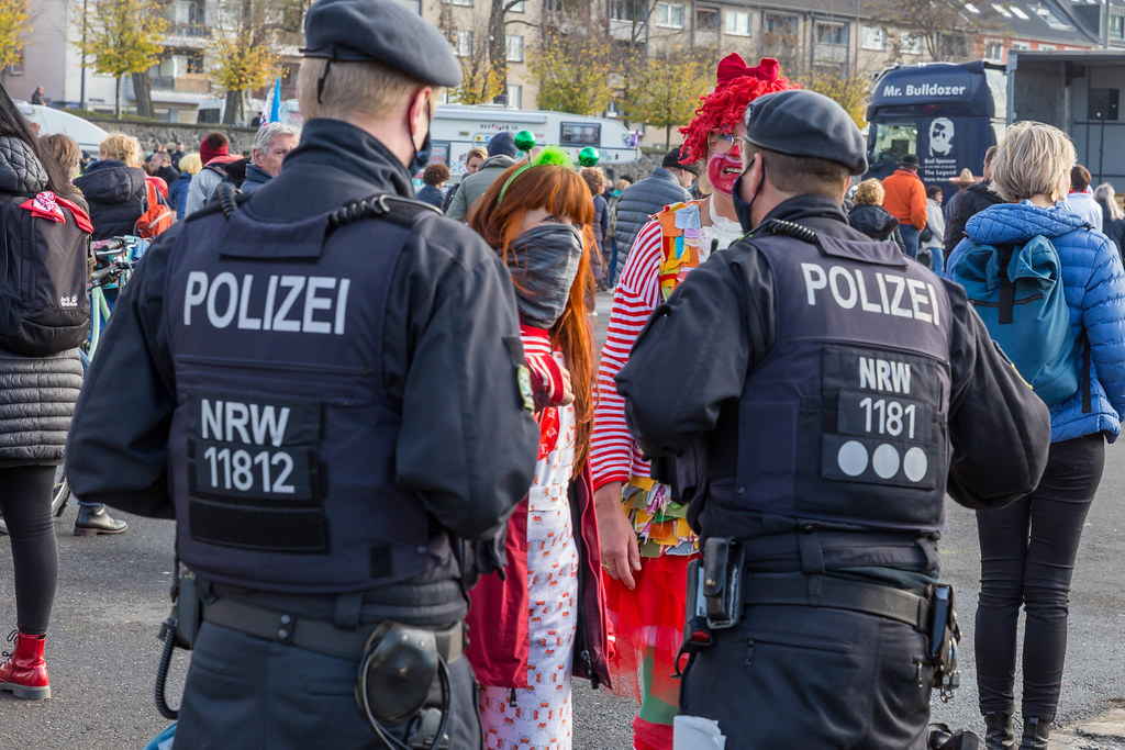 Two women in traditional Cologne red-white carnival costumes talk to the police at coronavirus protest