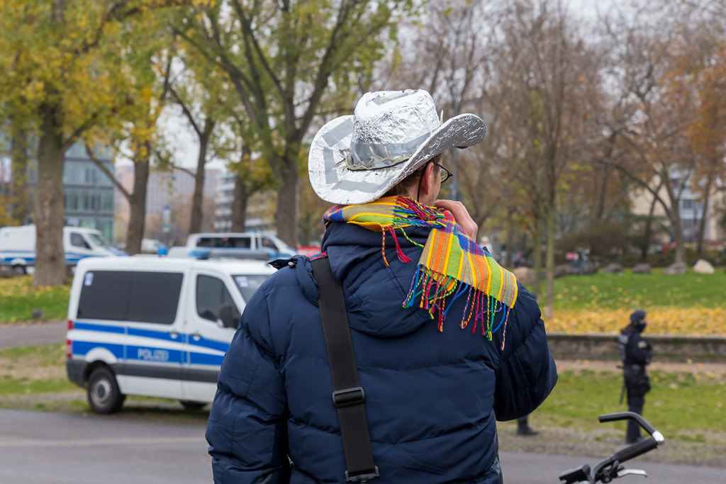 Mann mit Aluhut in Cowboy-Stil ohne Maske mit Polizeifahrzeug im Hintergrund. Anti-Corona-Demo