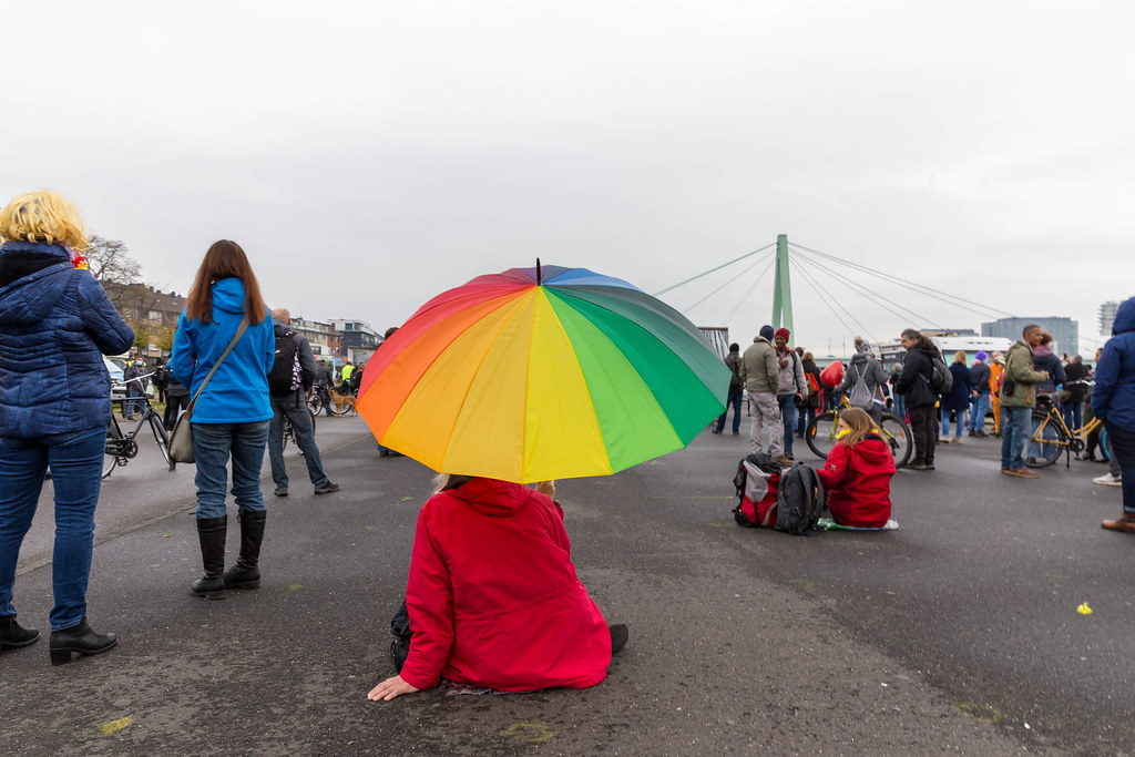 Deutzer Werft, Cologne: woman with rainbow umbrella, red jacket at demo against Covid-19 rules