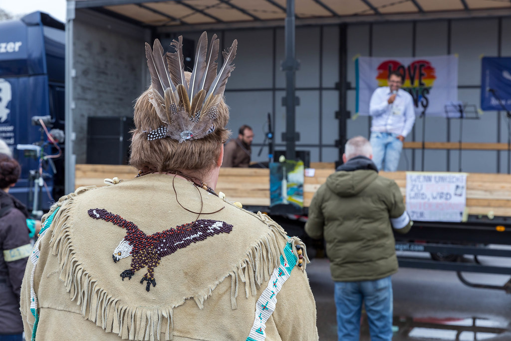 Mann als Indianer verkleidet hört dem Redner bei einer Anti-Corona-Demo auf Deutzer Werft in Köln zu
