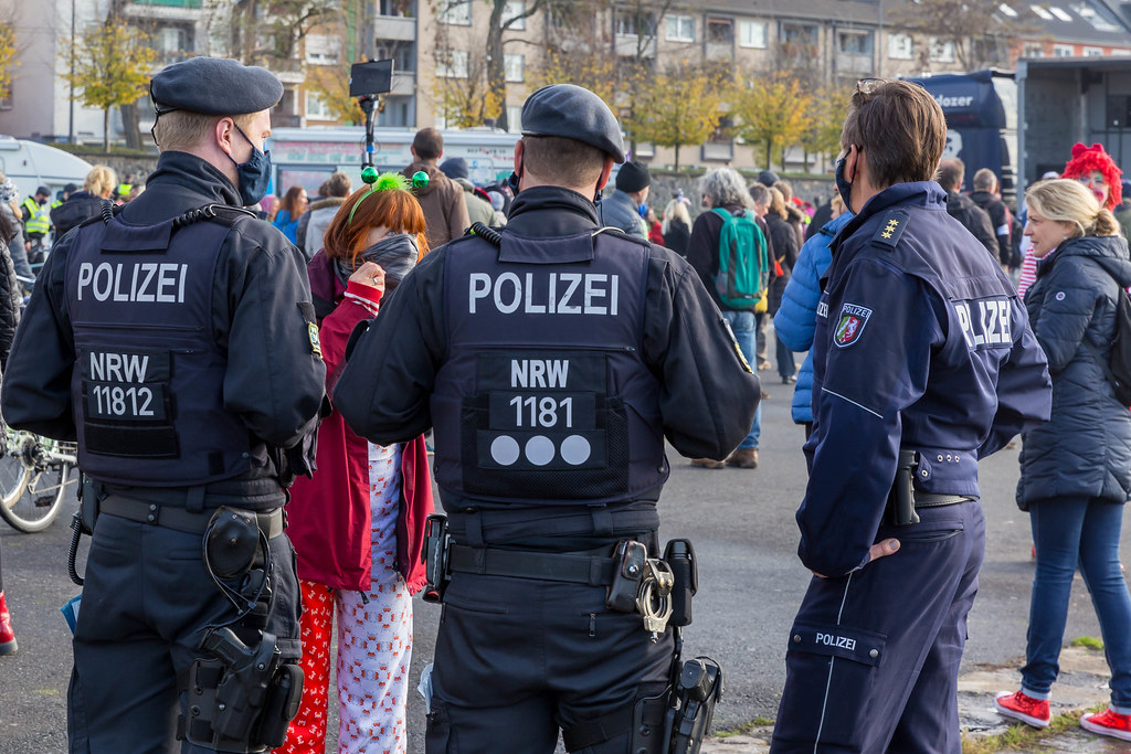 Drei Polizisten reden mit einer verkleideten Teilnehmerin bei der 11.11. Querdenker-Demo in Köln