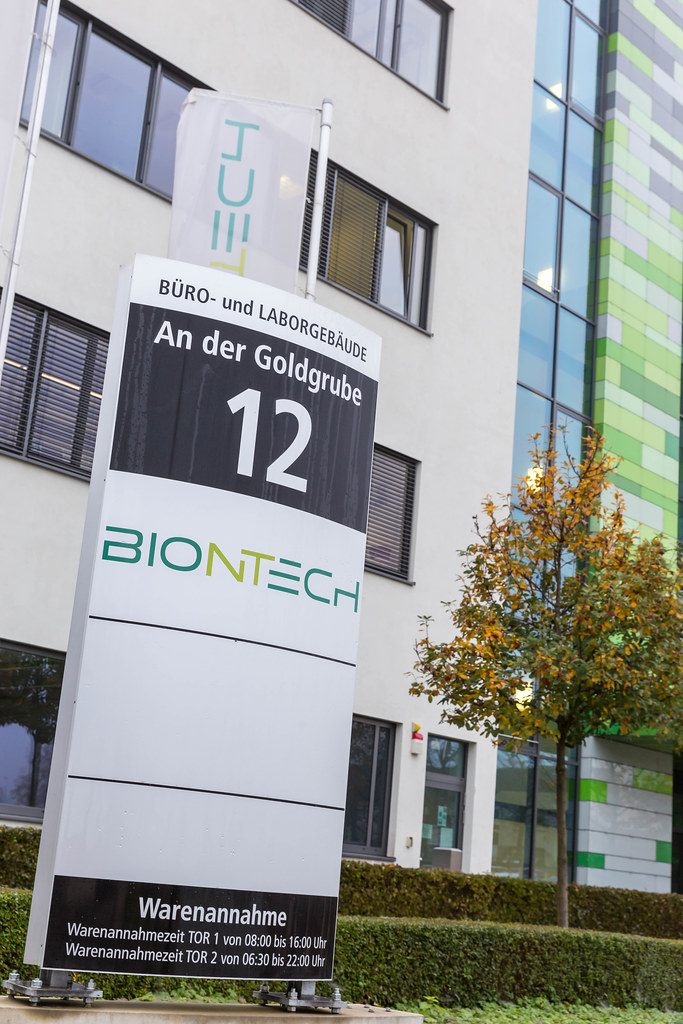 BioNTech Informations-Tafel mit Adresse An der Goldgrube 12 in Mainz und Warenannahme Öffnungszeiten mit BioNTech Gebäude und Flagge im Hintergrund