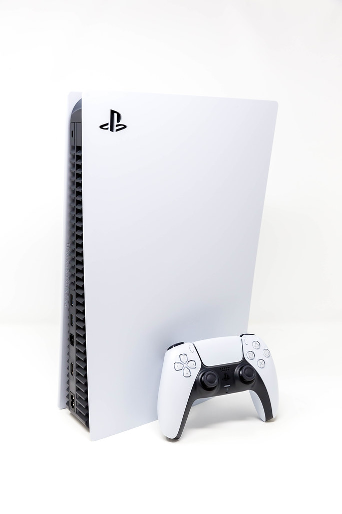 Eine stehende PlayStation 5 und der neue DualSense Wireless Controller vor weißem Hintergrund
