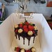 Buttercream covered chocolate drip cake adorned with chocolate and fresh soft fruits