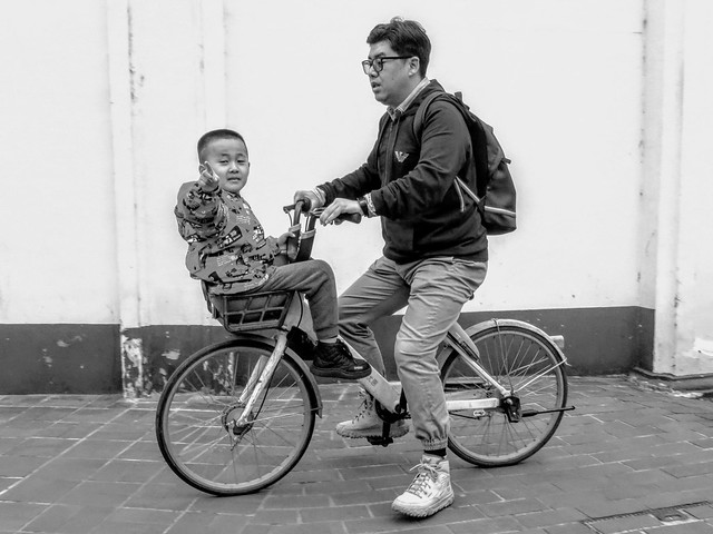 The son seems quite happy to be put in the basket of a shared bike by his father
