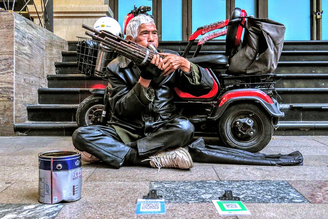 A disabled old man playing the sheng on the pavement in the city centre